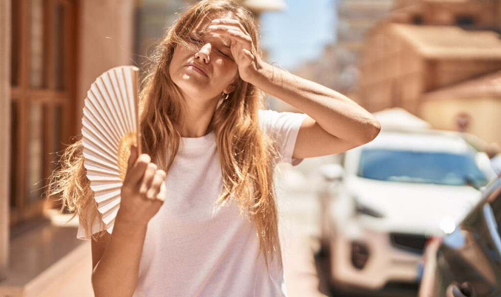 Young blonde girl using handfan at street