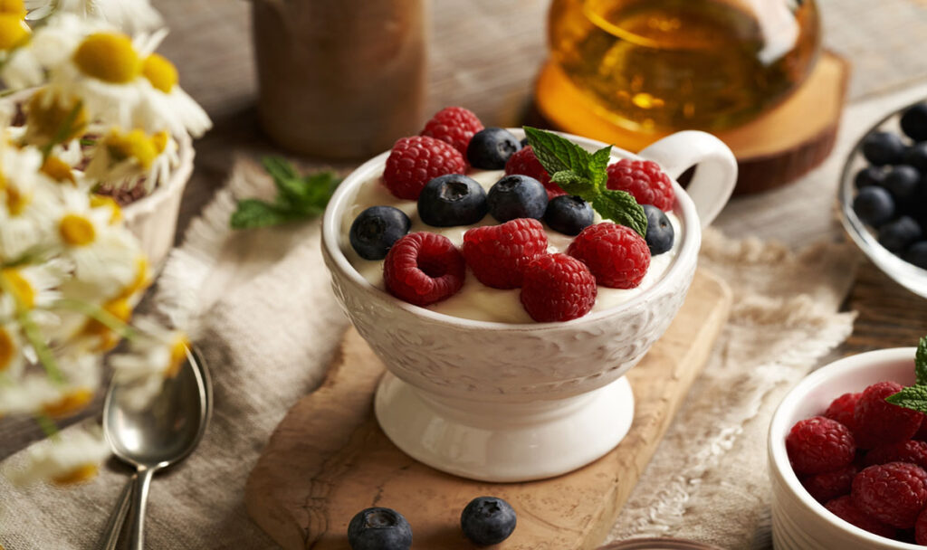 Cottage cheese blended with flax seed oil in a white cup in a bowl with fresh raspberries and blueberries