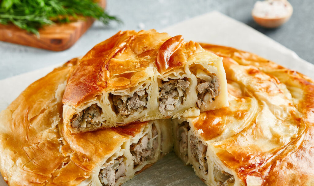 Classic turkish pie with meat on wooden board. Composition with burek pie on concrete background with textile and spices. Balkan pie with minced meat in rustic style on gray table