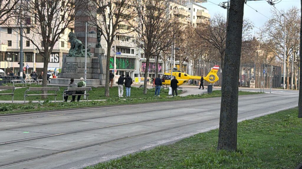 Hubschrauber OE-XVI auf Grünstreifen, Schaulustige, Denkmal im Hintergrund